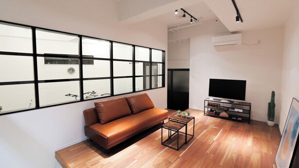 A modern living room with a leather sofa, a coffee table, a flat-screen TV, and a large window with black frames. - Casablanca Vacation House (Tokunoshima)