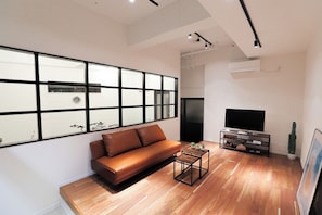 A modern living room with a leather sofa, a coffee table, a flat-screen TV, and a large window with black frames. - Casablanca Vacation House (Tokunoshima)