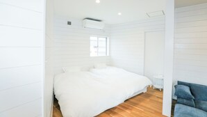 A bedroom with a large bed, a window, a white air conditioning unit, and a blue sofa. - Casablanca Vacation House (Tokunoshima)
