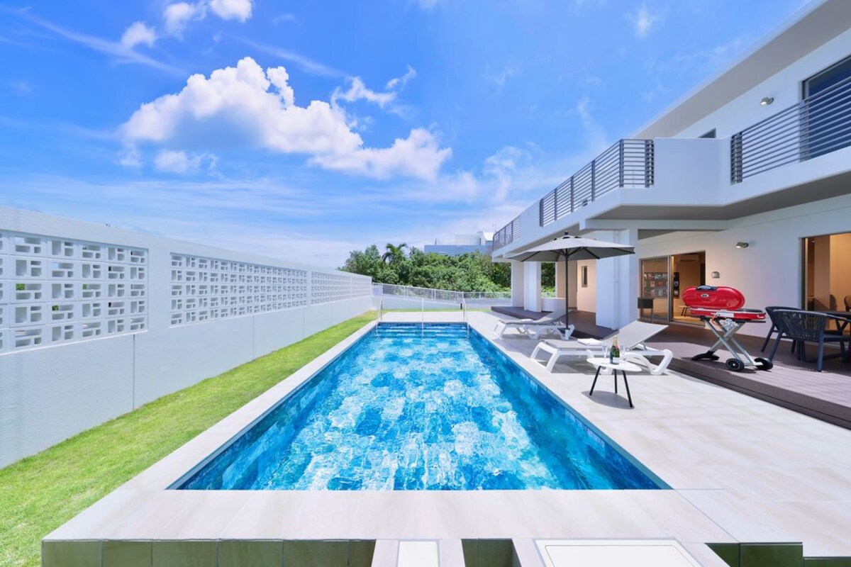 Piscina ao ar livre moderna com espreguiçadeiras e área para churrasco.