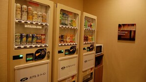 Máquinas de venda automática com bebidas e snacks, um micro-ondas e uma pequena cesto de roupa.