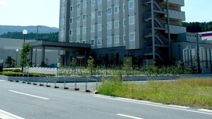 Hotel com vários andares e design moderno, com uma entrada imponente e área de estacionamento à frente.