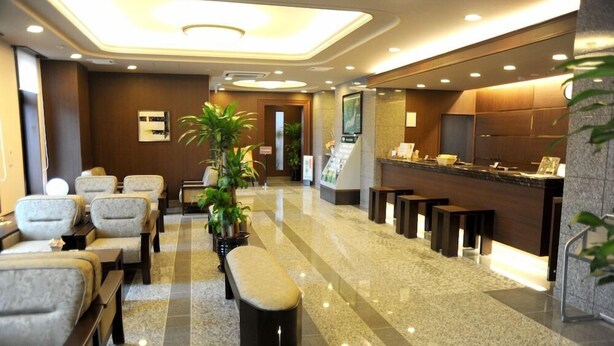Um saguão de hotel com assentos, balcão de recepção e uma planta.
