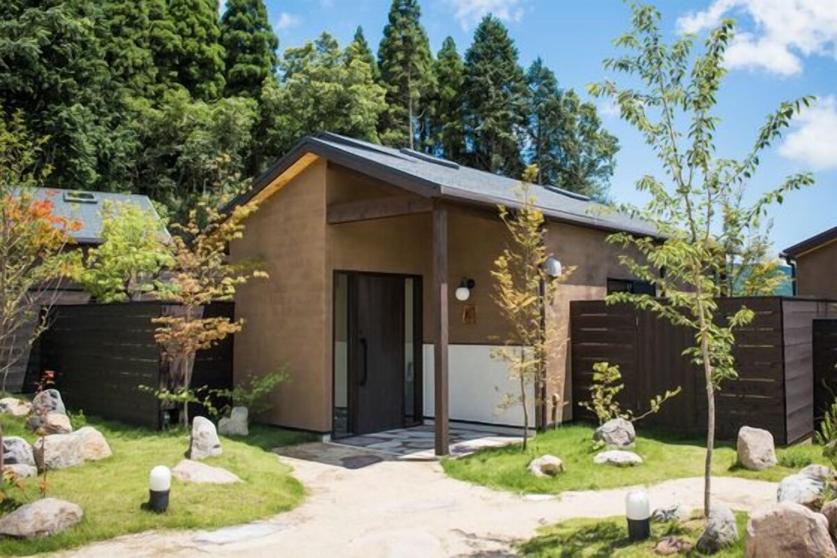 A modern building with a covered entrance, surrounded by a landscaped garden with rocks and trees.
