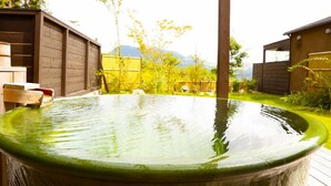 A hot tub in a garden with wooden cabins in the background. - Toki Resort Yufuin Villa (Yufu)