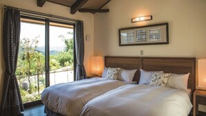 A double bed with a wooden headboard, a bedside table with a lamp, and a view of greenery through a large window. - Toki Resort Yufuin Villa (Yufu)