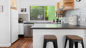 Cocina moderna con armarios blancos, una isla grande con taburetes, lavavajillas y ventana con vistas a la vegetación.