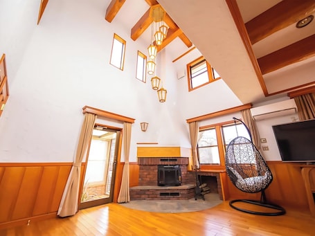 A spacious living room with wooden floors, a fireplace, a television, and a hanging chair.