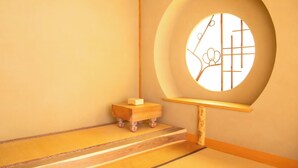 Een traditionele Japanse kamer met tatami vloeren, een lage houten kruk en een rond raam met decoratief ontwerp.