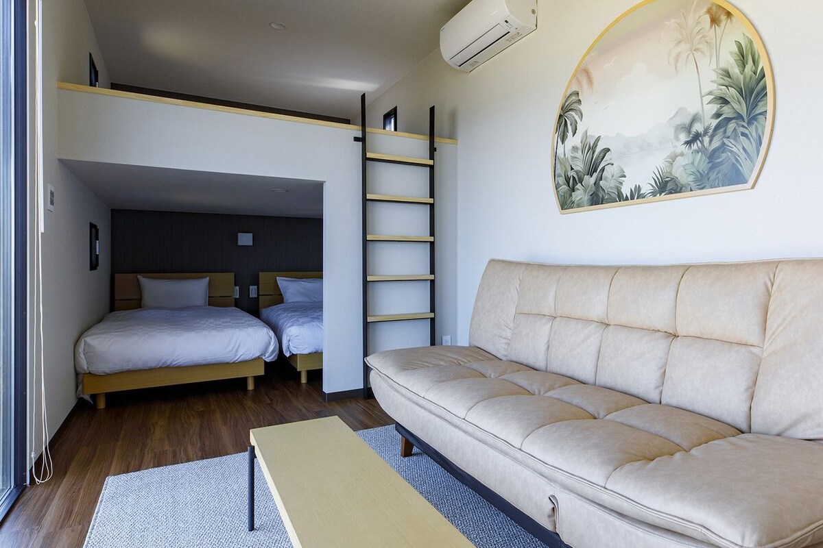 A bedroom with a bunk bed, a sofa, a ladder, and a painting on the wall.