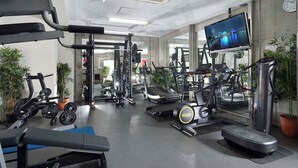 Un gimnasio con diverso equipo de ejercicio, un espejo grande y un televisor mostrando un paisaje urbano.