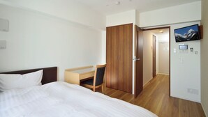 Habitación de hotel con cama, escritorio, silla, armario, televisor y panel de control.