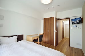 Une chambre d’hôtel équipée d’un lit, d’un bureau, d’une chaise, d’une armoire, d’un téléviseur et d’un panneau de commande.