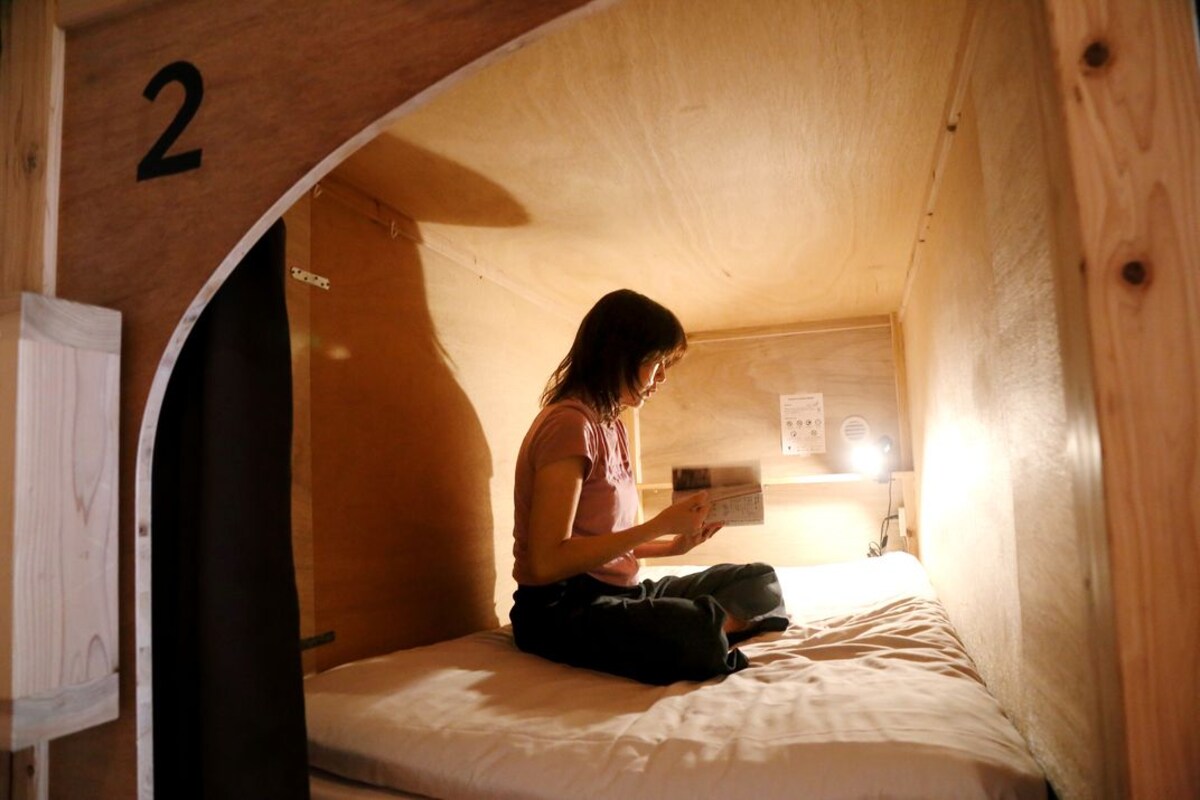 A small, cozy room with a wooden interior, a bed, and a person reading a book.
