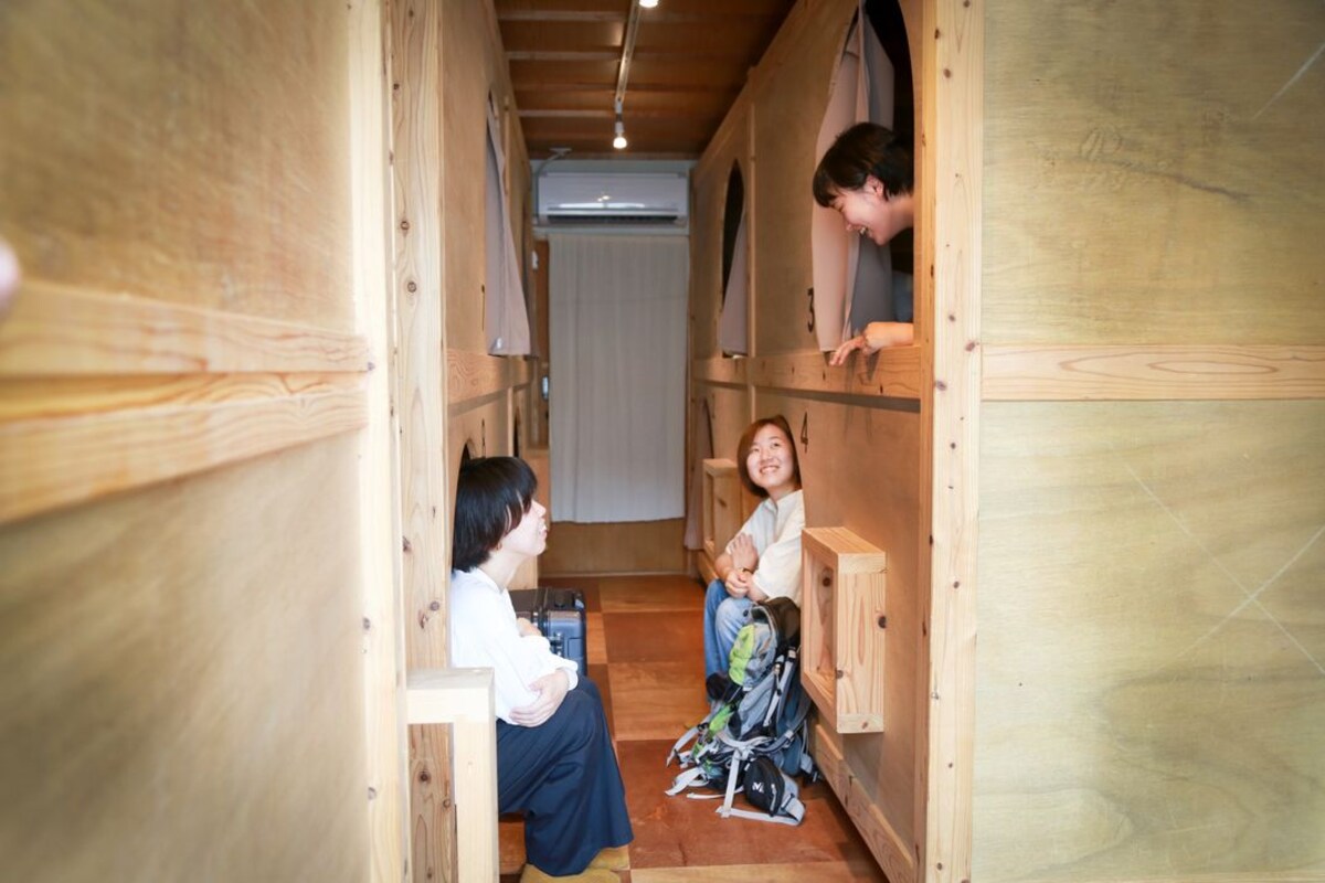 A wooden interior with a narrow passageway, a child with a stroller, and a person leaning out of a window.