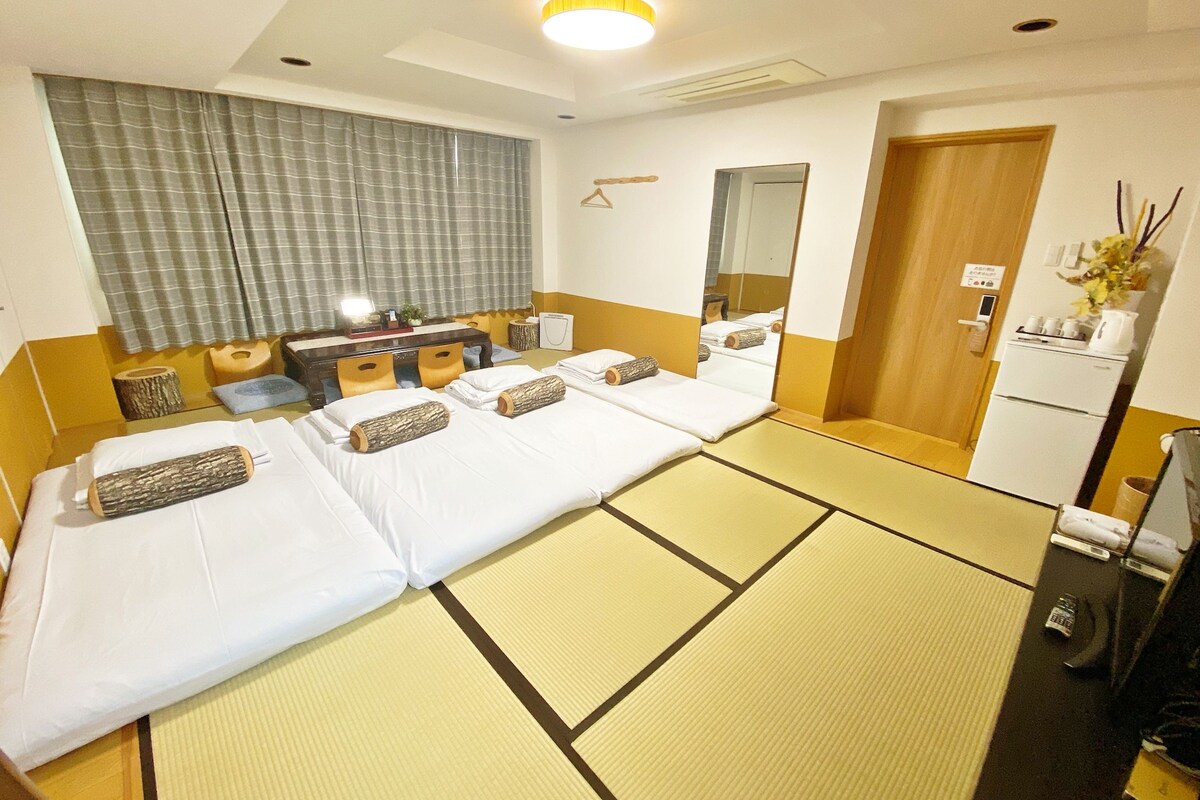 A hotel room with two beds, a desk, a mirror, a wardrobe, and a small kitchenette.