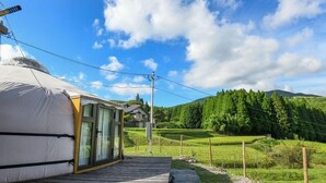 Eine Jurte mit einer Holzdielen-Terrasse, umgeben von terrassierten Feldern und einem Berg im Hintergrund.