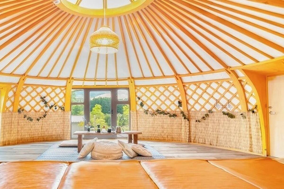A yurt with a central seating area, a hanging light fixture, and a view through the entrance.