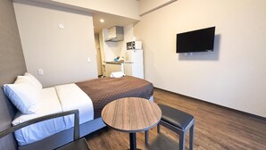A hotel room with a bed, a small round table, a chair, a TV mounted on the wall, and a kitchenette in the background. - Mr. Kinjo Link in Kume Naha (Naha)