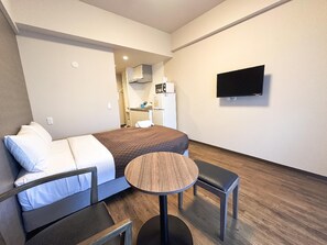 A hotel room with a bed, a small round table, a chair, a TV mounted on the wall, and a kitchenette in the background. - Mr. Kinjo Link in Kume Naha (Naha)