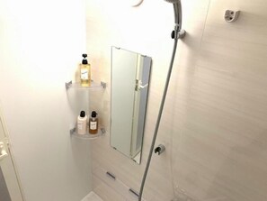 A bathroom with a shower, a mirror, and shelves with toiletries. - Mr. Kinjo Link in Kume Naha (Naha)