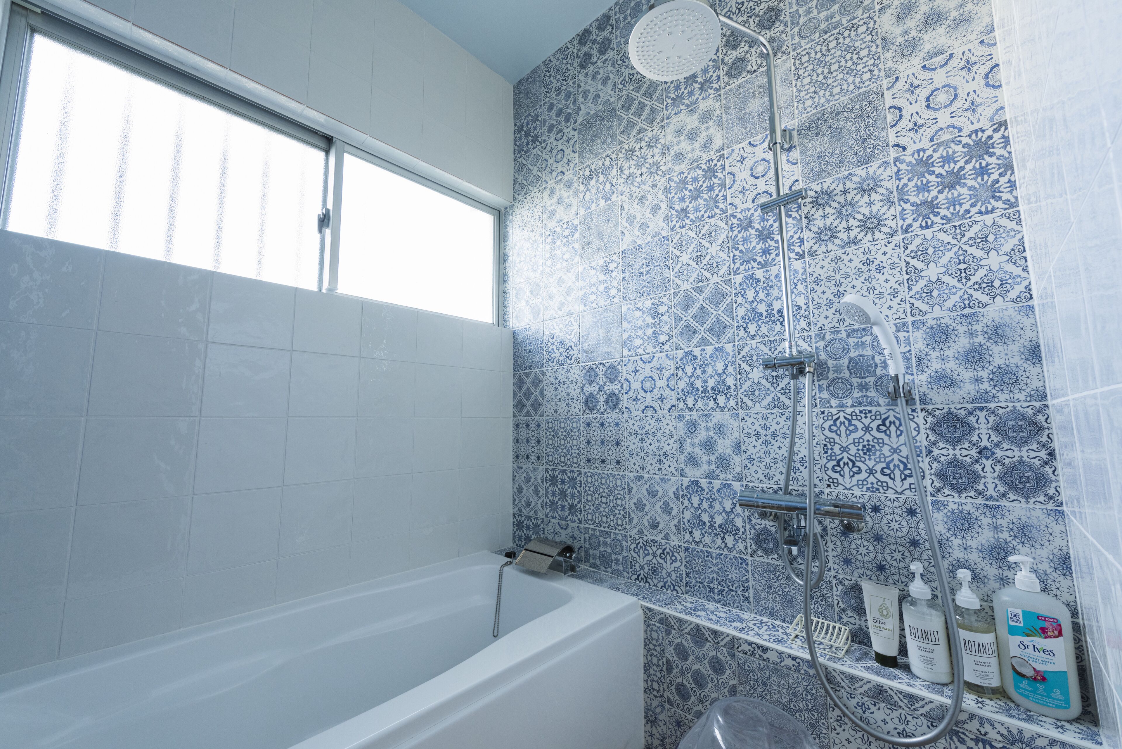 A bathroom with a bathtub, shower, and blue patterned tiles.