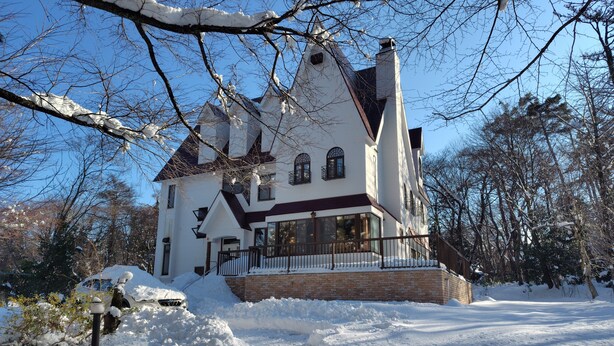 Une grande maison blanche à plusieurs étages, dotée d’un toit en pente et entourée d’arbres couverts de neige.