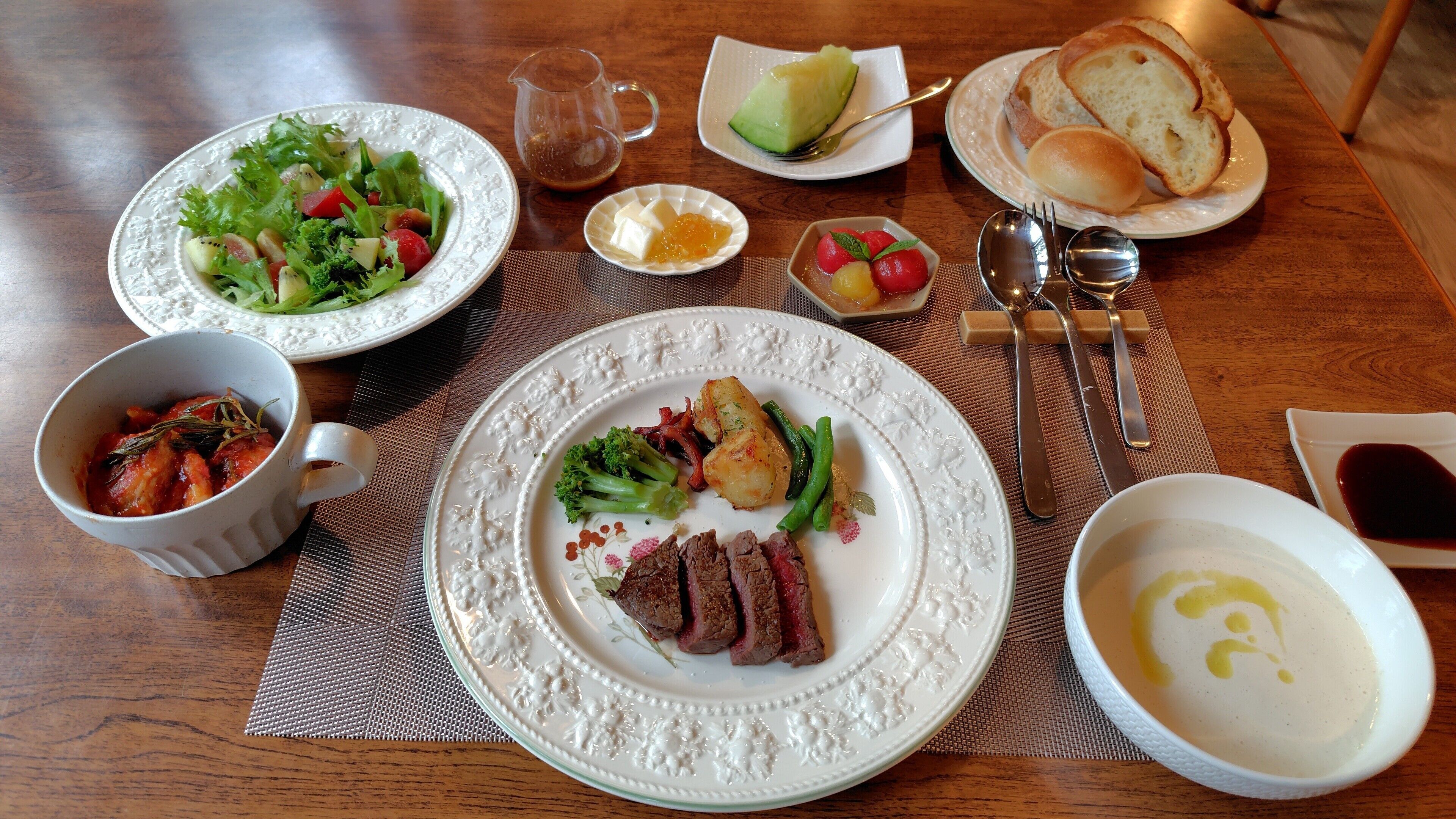 Une table à manger avec des assiettes remplies de nourriture, des couverts et un bol de soupe.