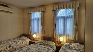 Une chambre avec deux lits simples, chacun doté d’une table de chevet et d’une lampe de chevet. La chambre est équipée d’une fenêtre avec des rideaux et d’un climatiseur mural.