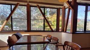 Un coin repas avec une table en verre et des chaises en bois, de grandes fenêtres donnant sur la verdure et un mur en briques.