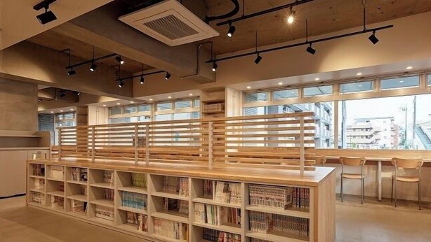 L’intérieur d’une bibliothèque moderne, avec des étagères en bois, un espace de lecture central et de grandes fenêtres laissant entrer la lumière naturelle.