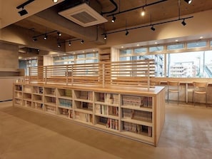 A modern library interior with wooden bookshelves, a central seating area, and large windows allowing natural light. - Lil Beats Inn Wakaba Higashiguchi (Sakado)