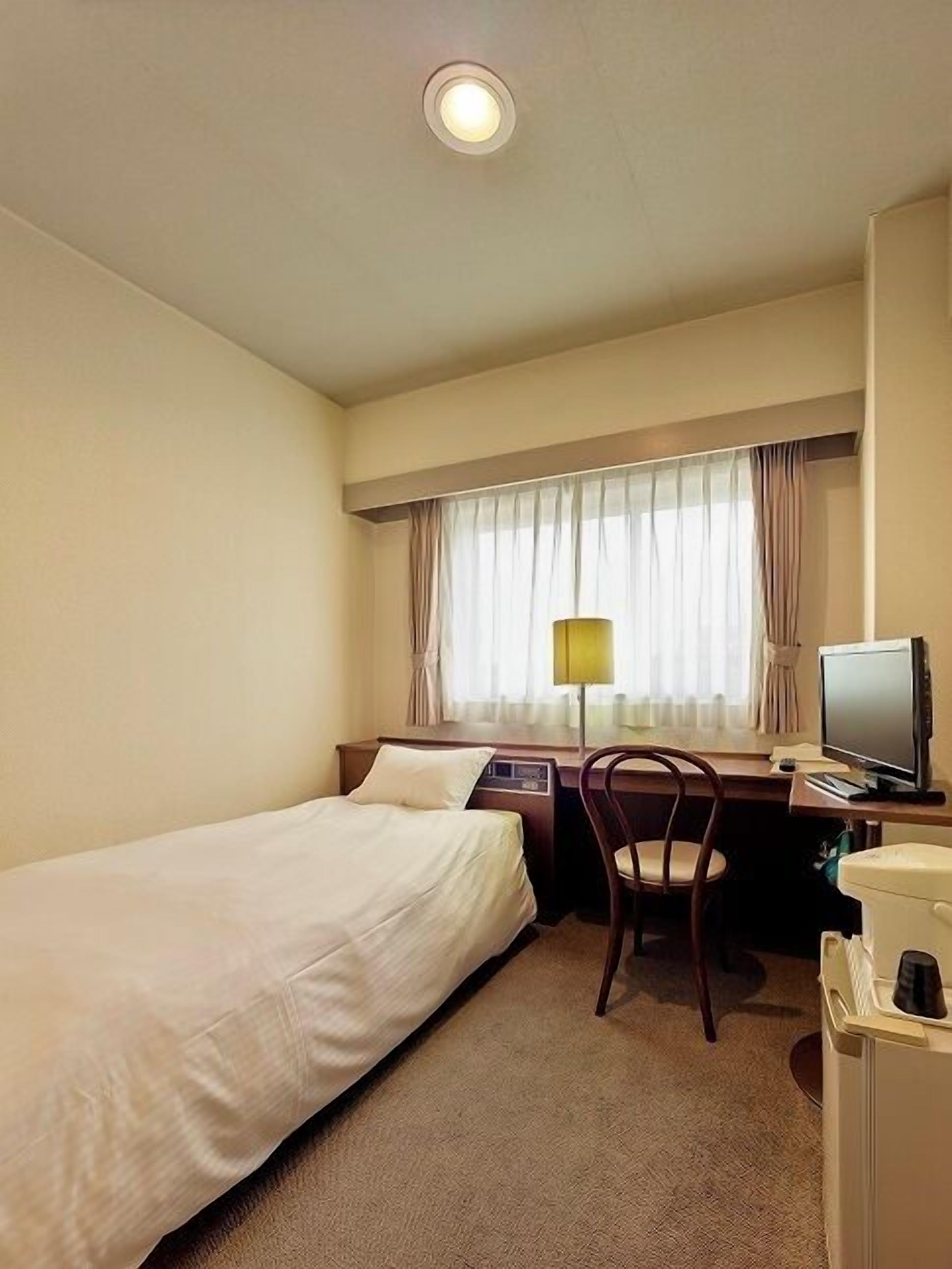 Habitación de hotel con dos camas individuales, un escritorio con silla, televisor y ventana con cortinas.