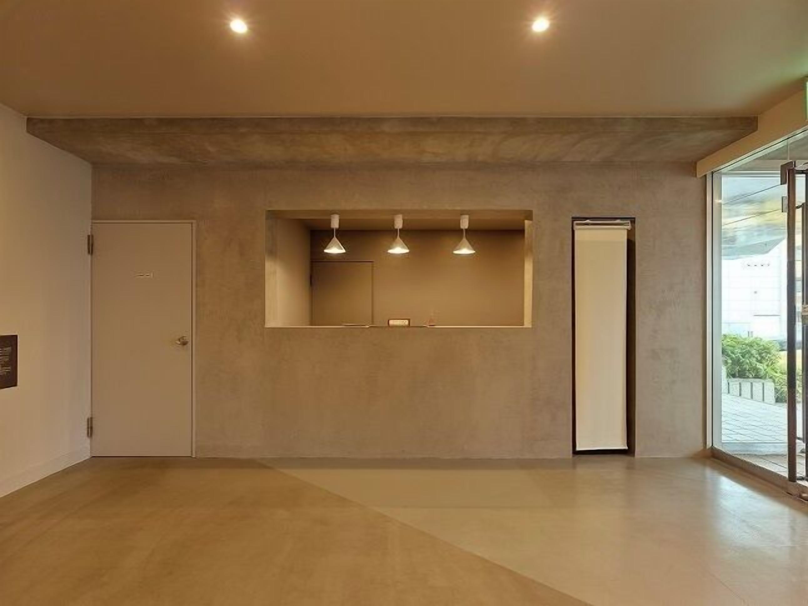 Un interno moderno con un design minimalista, che include una reception con illuminazione a sospensione, un grande specchio e una porta che dà su un balcone.