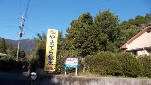 Un letrero amarillo con texto en japonés, un letrero más pequeño con símbolos, y un edificio al fondo.