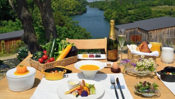 A table set for breakfast with a scenic river view, including fruits, vegetables, bread, and beverages. - Tobe Auberge Resort (Tobe)
