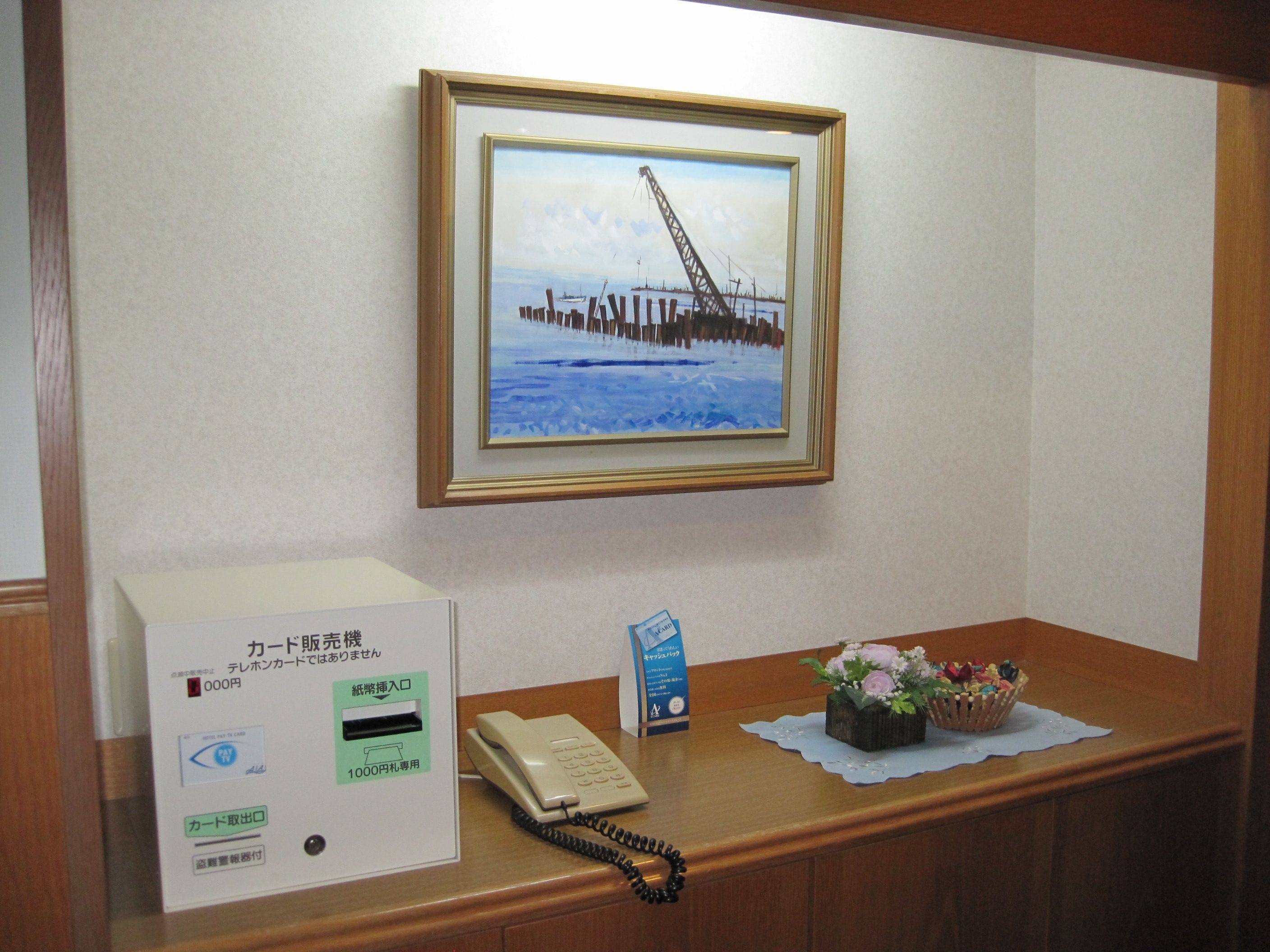 A reception desk with a framed picture of a bridge, a telephone, a card reader, and a small flower arrangement.