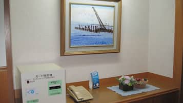 A reception desk with a framed picture of a bridge, a telephone, a card reader, and a small flower arrangement.