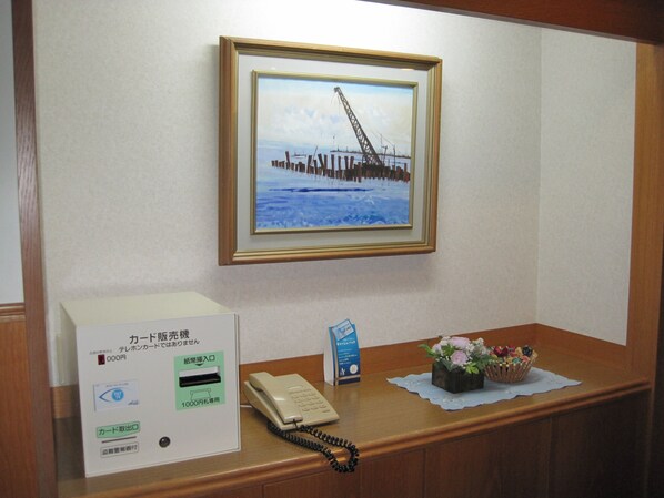 A reception desk with a framed picture of a bridge, a telephone, a card reader, and a small flower arrangement.
