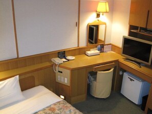 A hotel room with a bed, a desk with a telephone, a television, a mirror, and a small refrigerator.