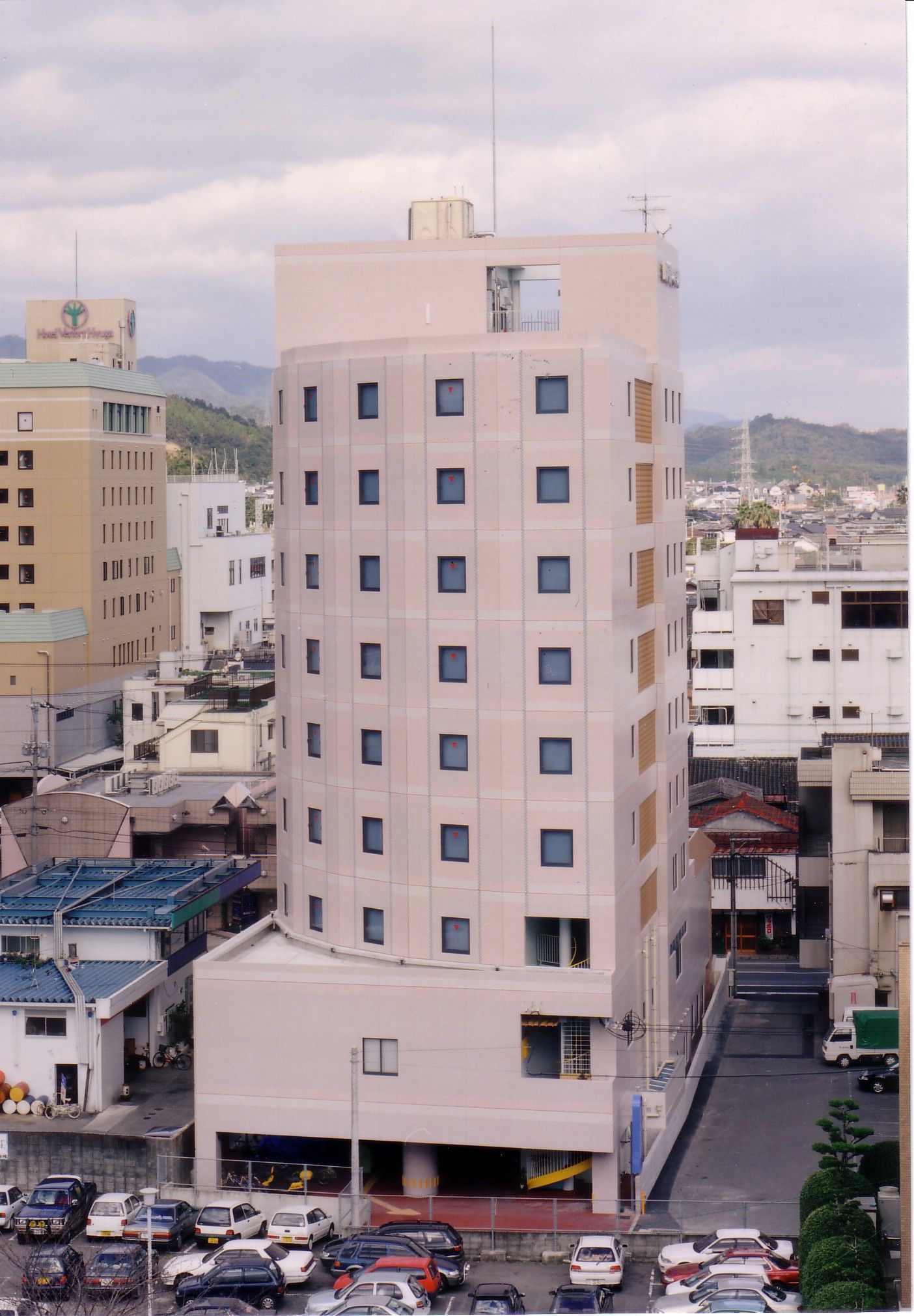 Un hotel de diverses plantes amb façana plana, nombroses finestres i una zona d'aparcament amb diversos cotxes.