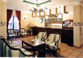 Comedor tradicional con mobiliario de madera, una araña y una zona de bar con libros y botellas.
