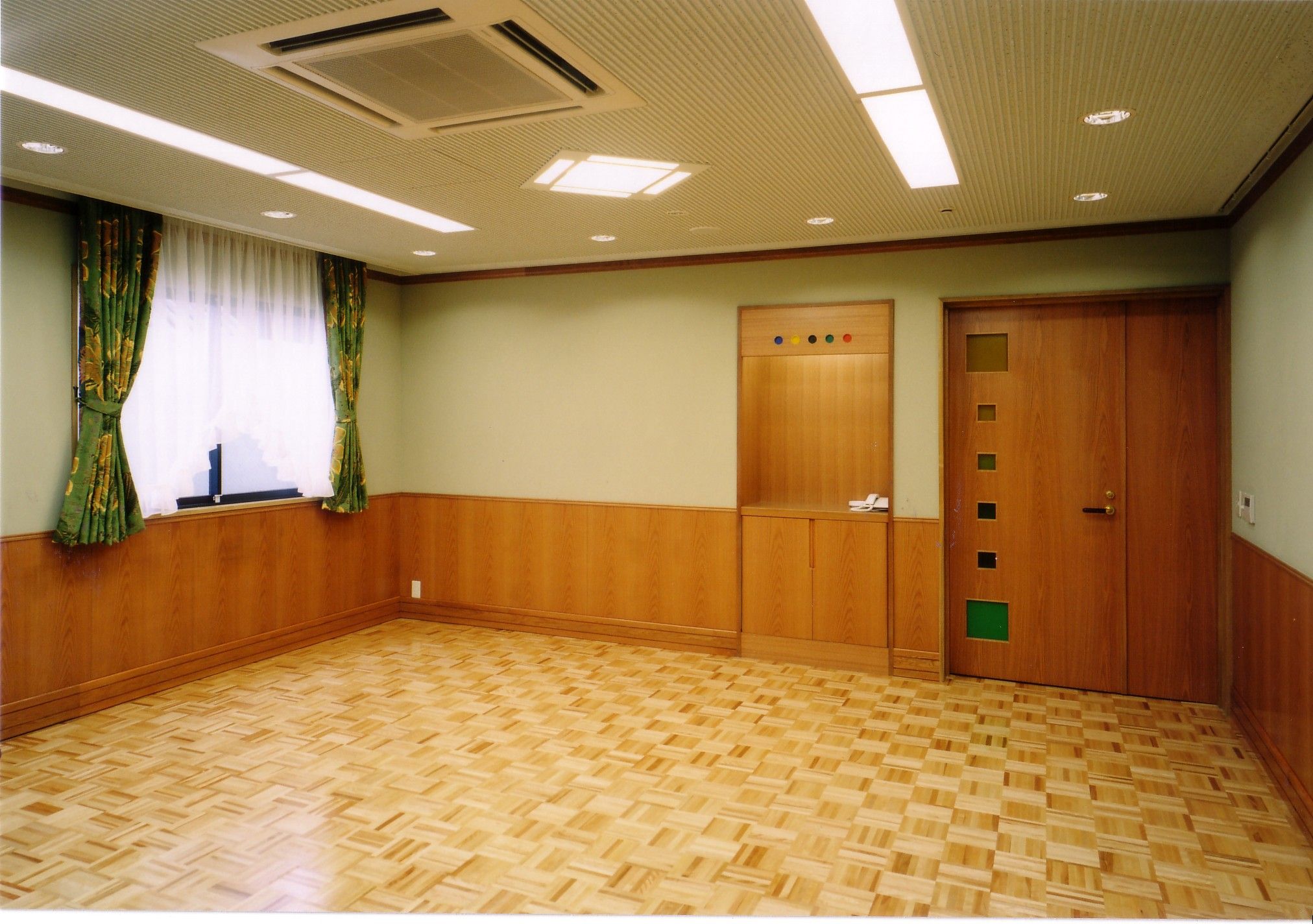 Ein Zimmer mit Holzboden, einem Fenster mit grünen Vorhängen und einer Tür mit Lichtschalter.