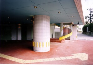 A building entrance with a tiled column, a yellow spiral staircase, and tactile paving for the visually impaired.