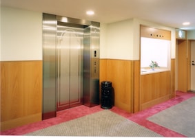 A hotel corridor with an elevator, a trash bin, and a window with a view.