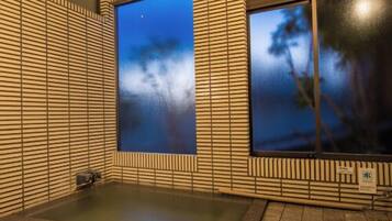 A modern bathroom with a large bathtub, a window with a view of trees, and a tiled floor.