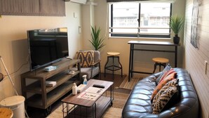 A modern living room with a flat-screen TV, a sofa, a coffee table, and a small dining area with stools. - Nemuru Kagoshima Chuo Eki (Kagoshima)