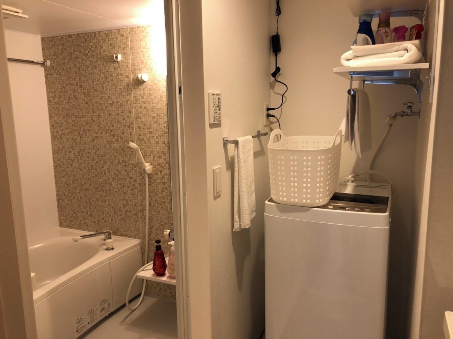 A compact bathroom with a shower, a small sink, and a washing machine.