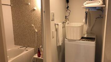 A compact bathroom with a shower, a small sink, and a washing machine.