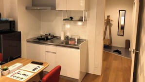 A compact kitchen with white cabinets, a gas stove, and a microwave. There is a dining area with a table and chairs, and a mirror on the wall. - Nemuru Kagoshima Chuo Eki (Kagoshima)